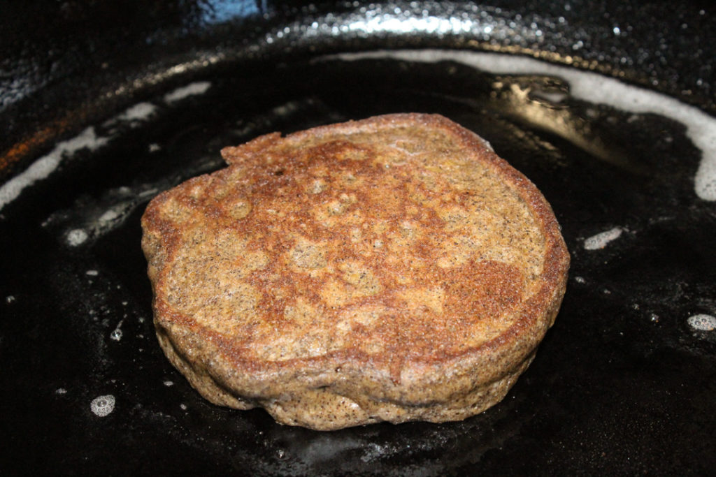 Gluten and dairy free pumpkin spice pancake cooking in a cast iron skillet.