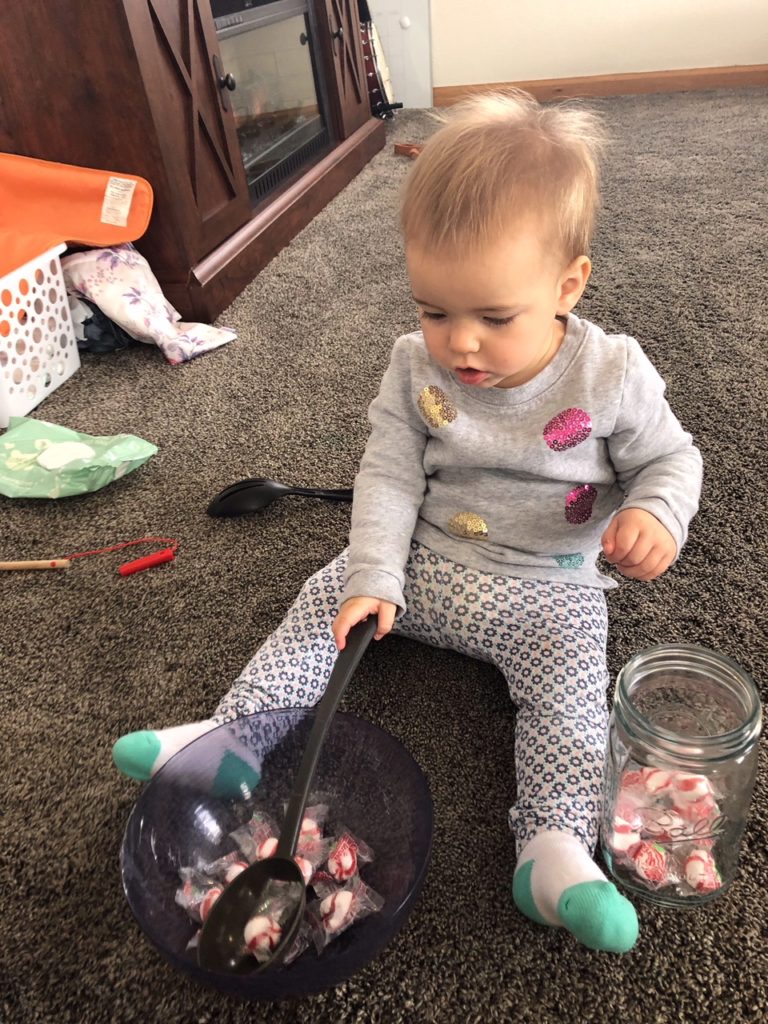 Toddler using eye movement skills to scoop peppermint candies out of a bowl using a ladle.